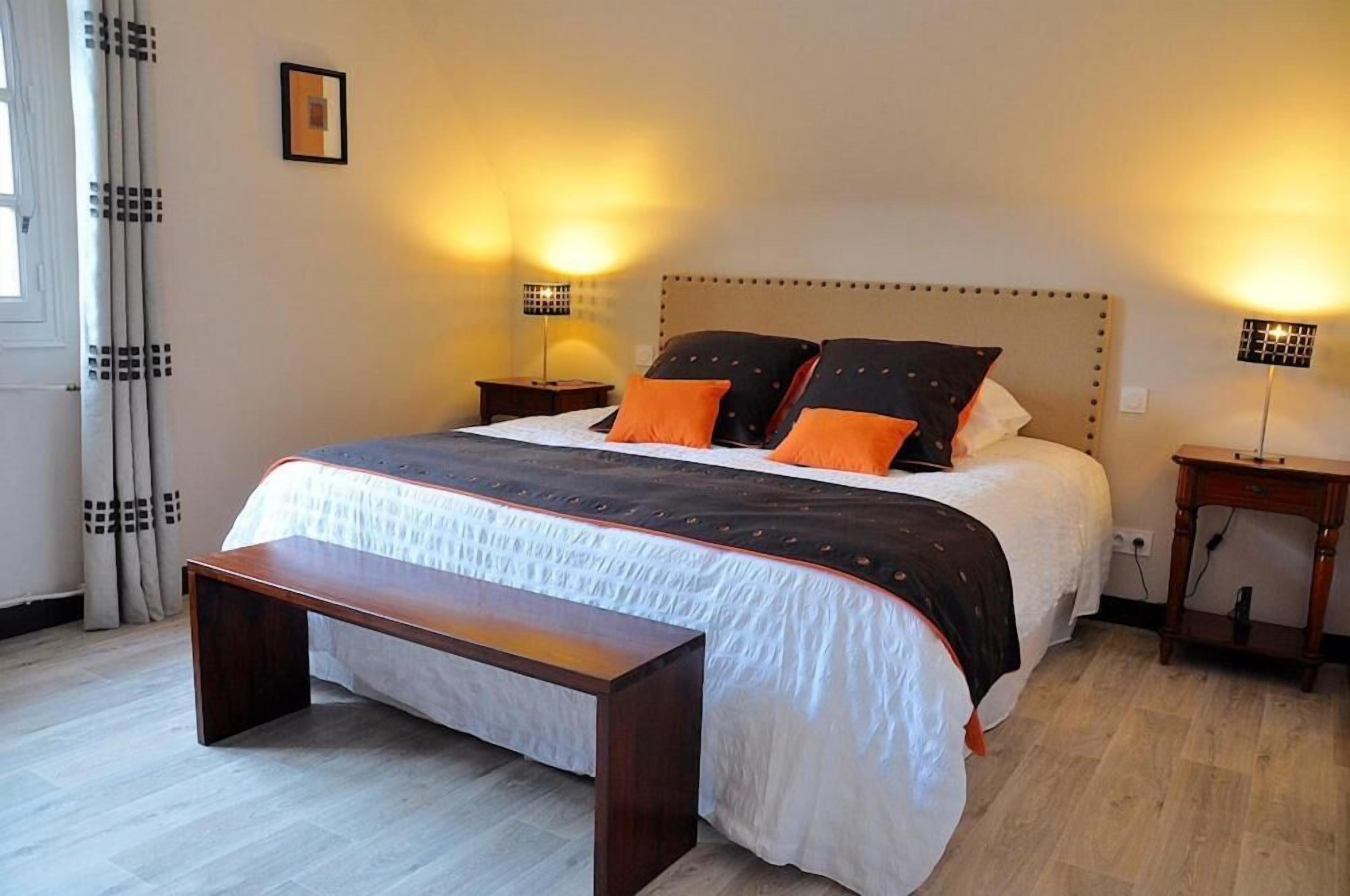 Un dormitorio ordenado con una cama grande, dos mesitas de noche y un banco.