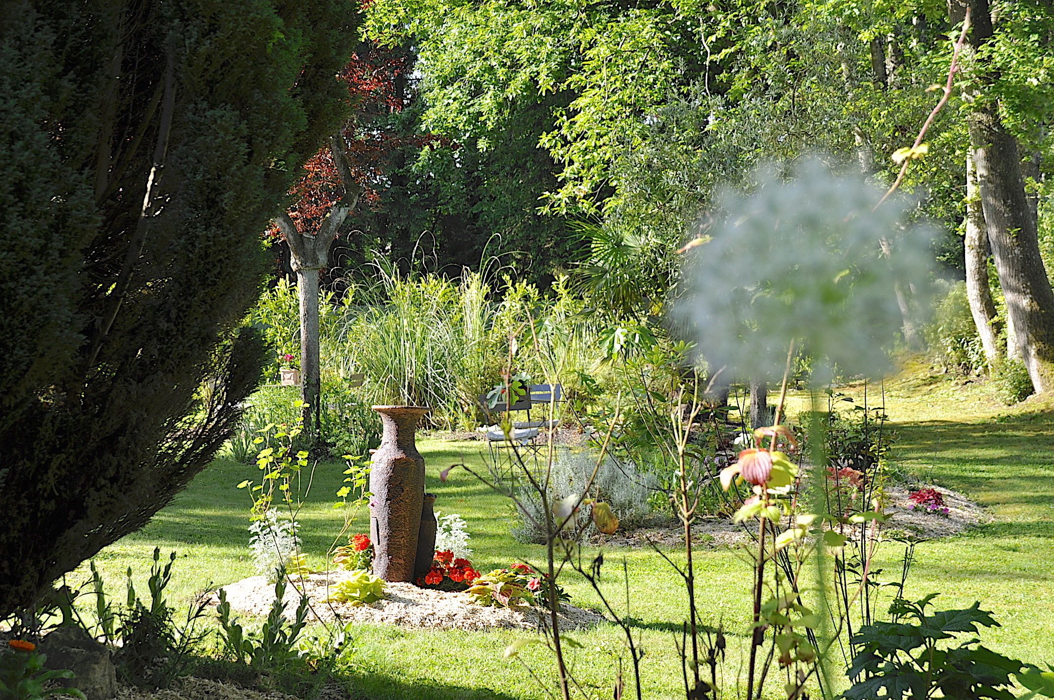 A garden with a large vase, various plants, and a bench.