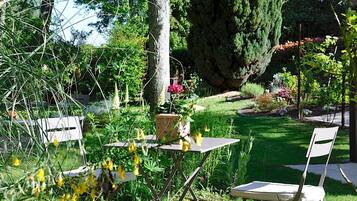 Un jardín al aire libre con una mesa y dos sillas, rodeado de diversas plantas y un árbol grande.