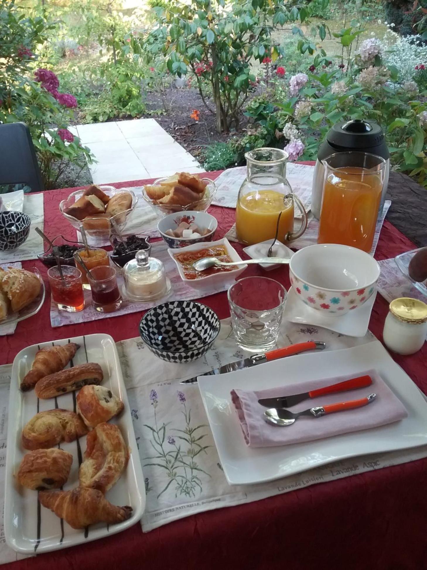 A breakfast table set outdoors with croissants, bread, fruit, and beverages.