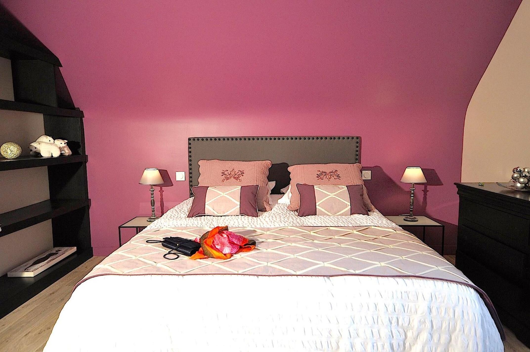A neatly made bed with a patterned bedspread, two bedside lamps, and a shelf with decorative items.