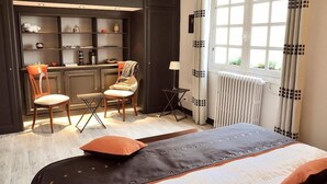 A modern hotel room with a large bed, two chairs, a small table, and a built-in desk with shelves. - Au Jardin de Lisa (Cherré-Au)