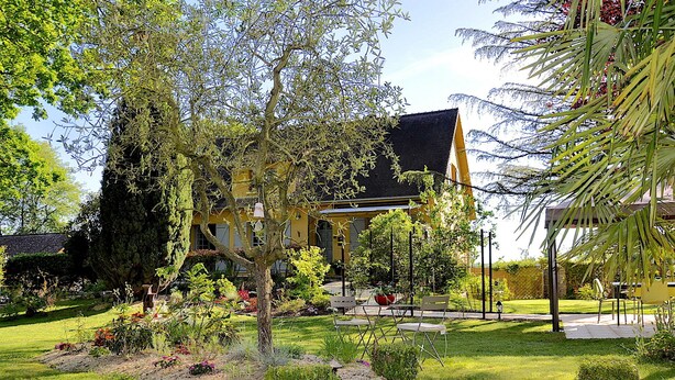 A yellow house with a black roof, surrounded by a well-maintained garden with various plants and a lawn. - Au Jardin de Lisa (Cherré-Au)