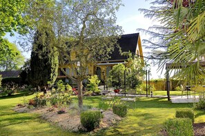 Una casa amarilla con techo negro, rodeada de un jardín cuidado con diversas plantas y césped.