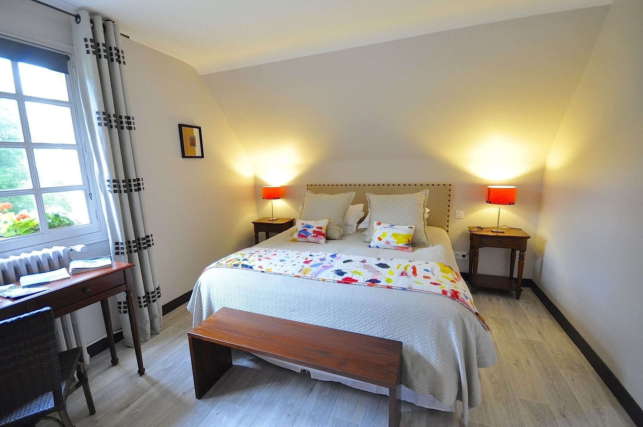 A bedroom with a bed, bedside tables, a desk, a bench, and a window with curtains.