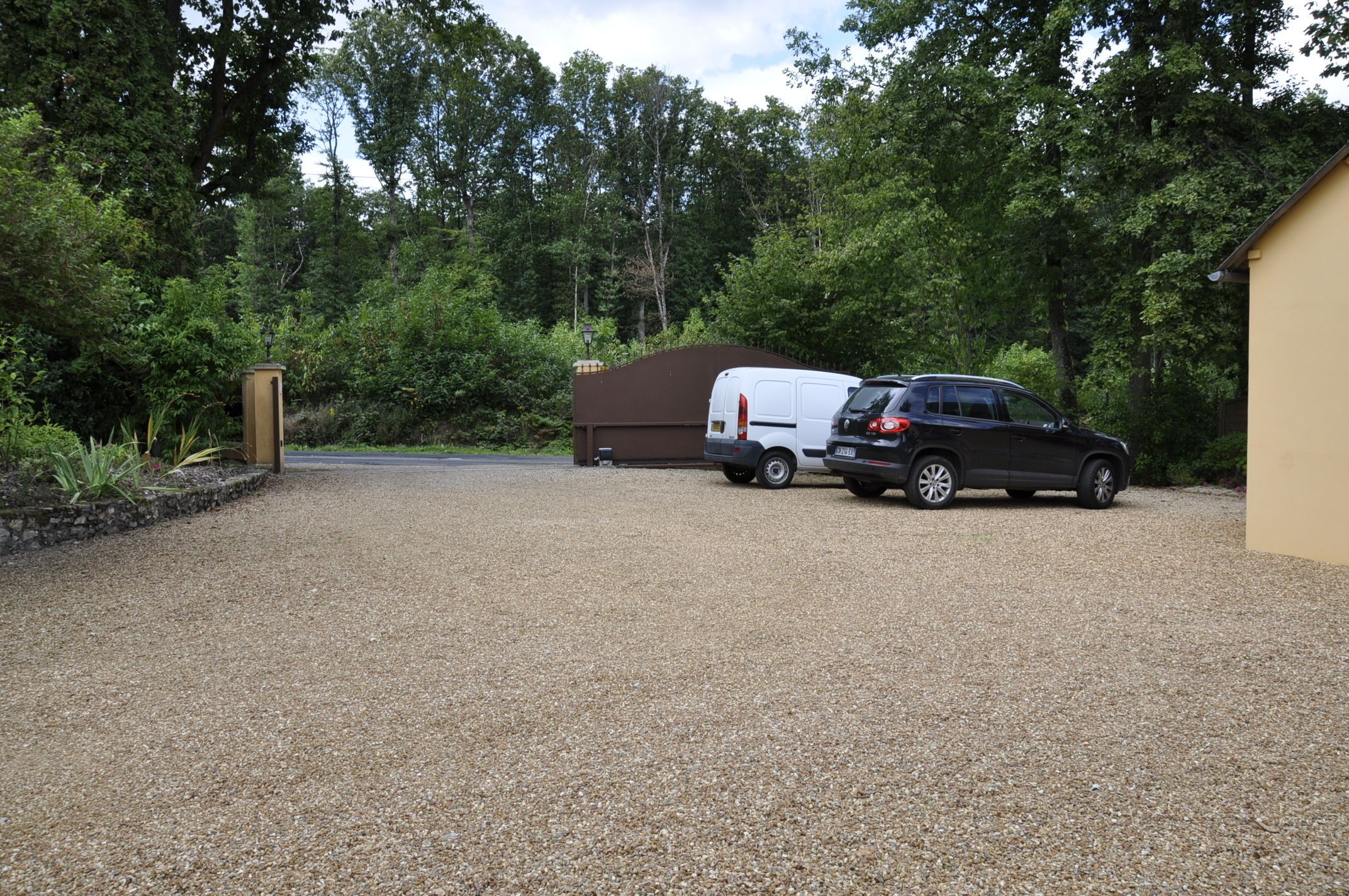 A gravel driveway leading to a house with a white trailer parked in the driveway.