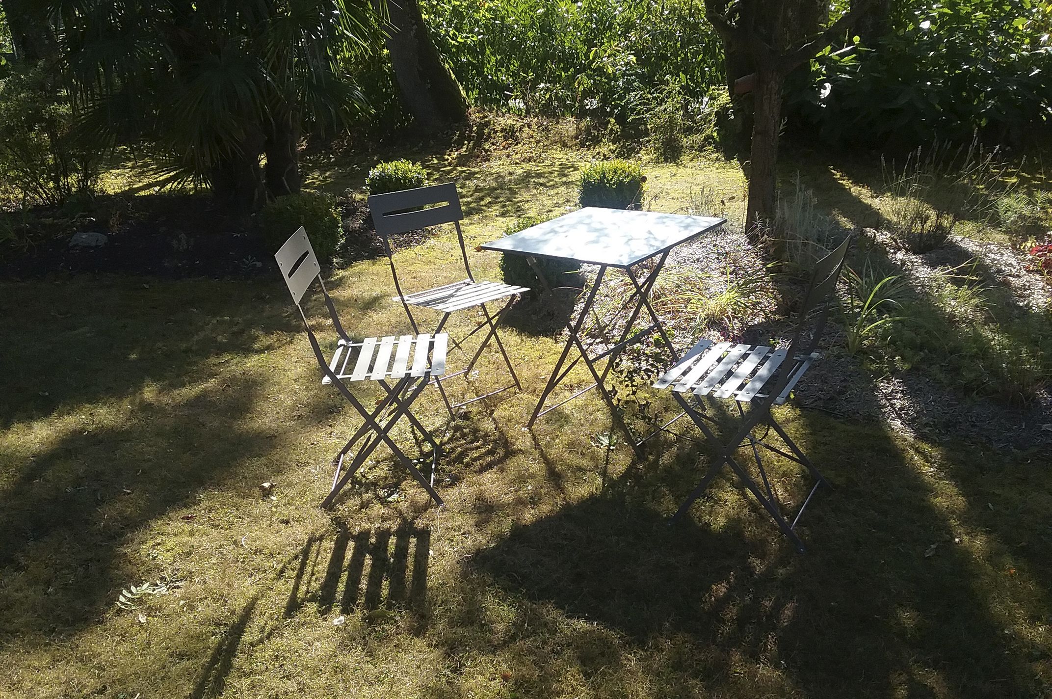 An outdoor seating area with a table and two chairs, surrounded by greenery and trees.