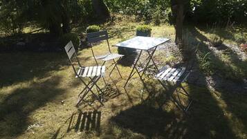 An outdoor seating area with a table and two chairs, surrounded by greenery and trees.