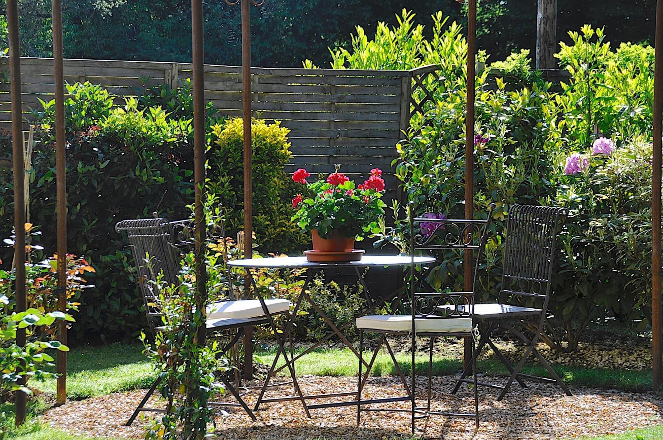 A garden with a table and chairs, surrounded by various plants and flowers.
