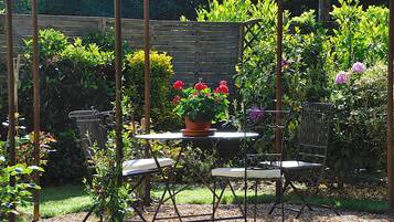 A garden with a table and chairs, surrounded by various plants and flowers.