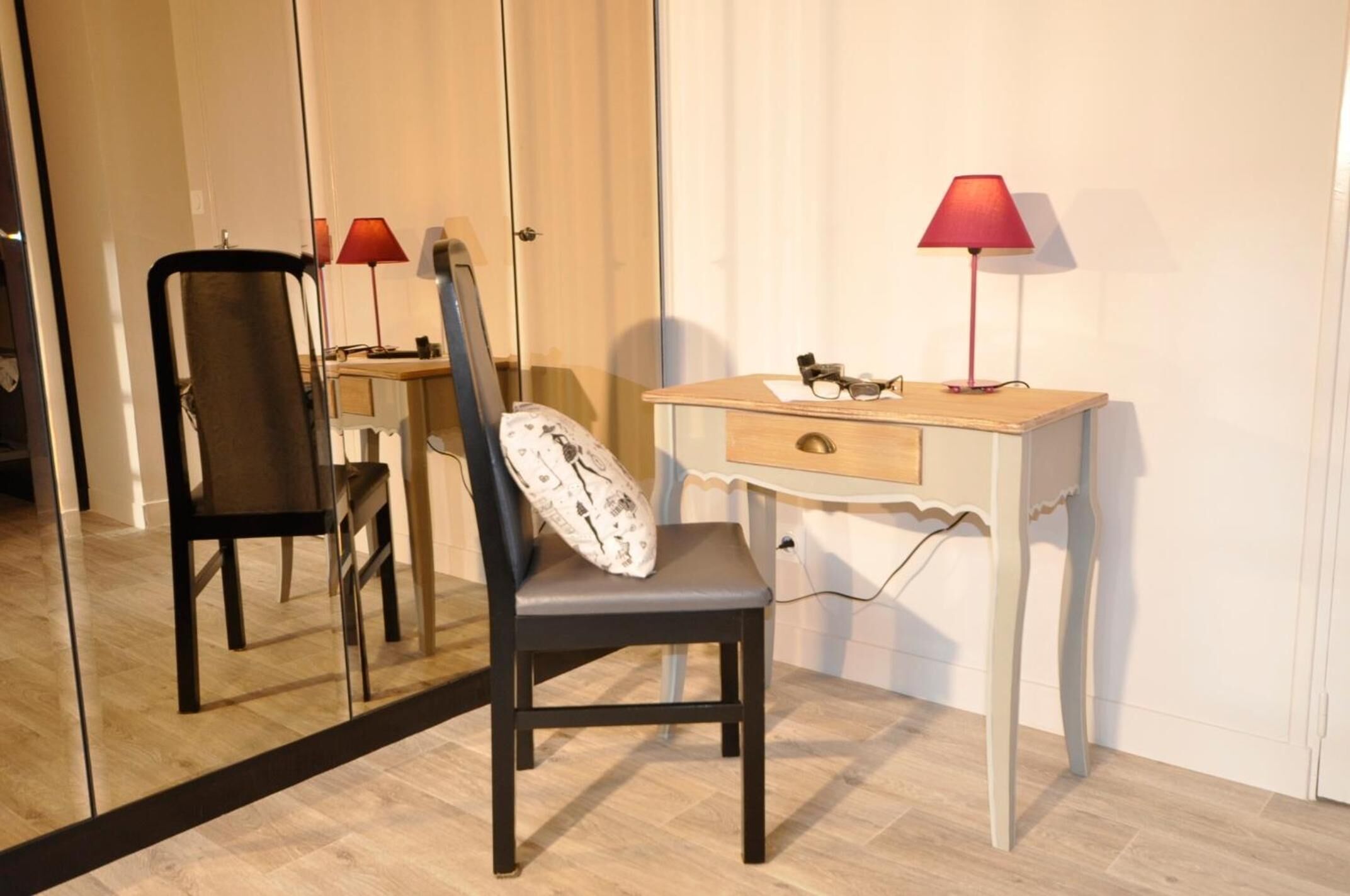 A bedroom with a bed, a bedside table with a lamp, a chair, and a mirror.