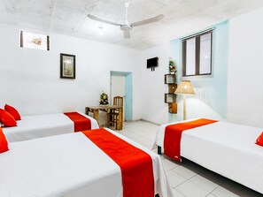 A hotel room with two beds, each with a red and white bedspread, a ceiling fan, a small table with a vase of flowers, and a wall-mounted TV.