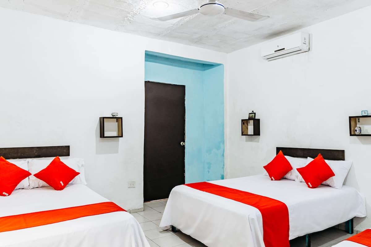 A hotel room with three beds, white bedding, red accents, and a blue door.