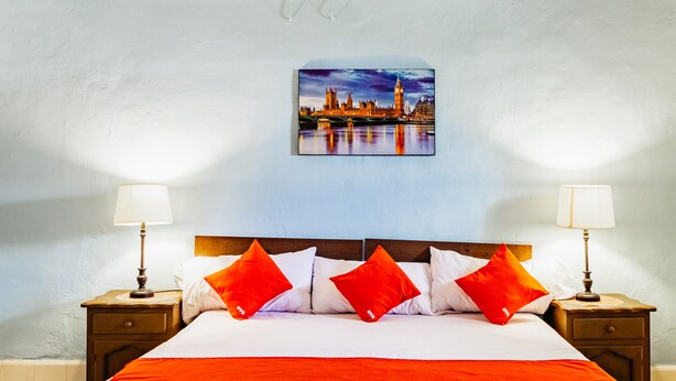 A hotel room with a large bed, two bedside tables, and a cityscape painting on the wall. - Hotel Casa Lidia (Mérida)