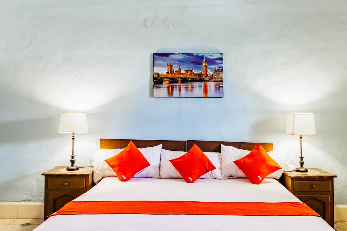 A hotel room with a large bed, two bedside tables, and a cityscape painting on the wall.