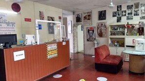A hotel reception area with a wooden reception desk, a red chair, and a wall decorated with various posters and pictures. - Hotel Casa Lidia (Mérida)