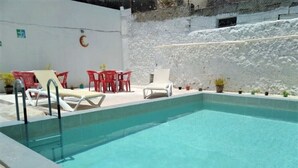 A swimming pool with lounge chairs and tables, surrounded by a white wall and a stone wall. - Hotel Casa Lidia (Mérida)