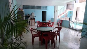 A dining area with a round table and red plastic chairs, surrounded by potted plants. - Hotel Casa Lidia (Mérida)