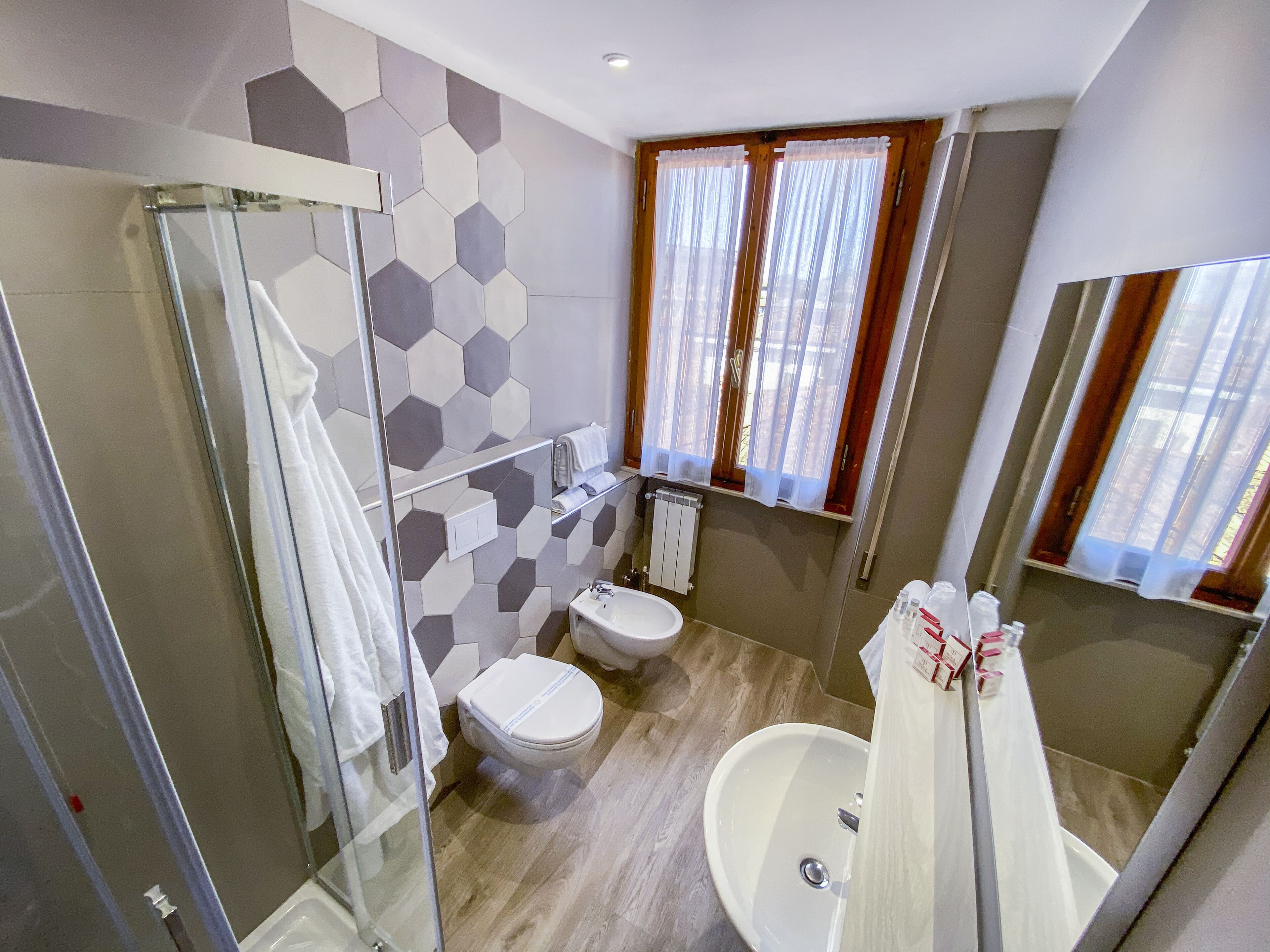 Un baño con cabina de ducha de vidrio, inodoro, lavabo y ventana con cortinas.