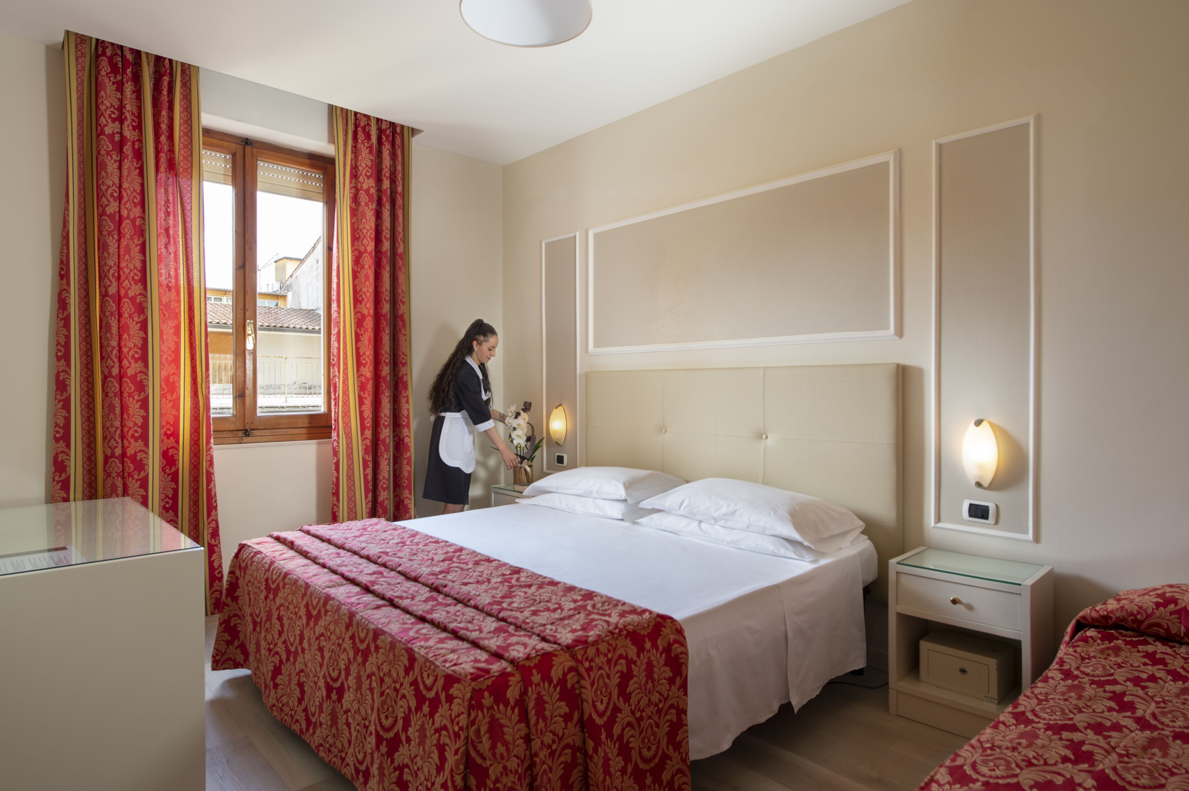 Ein Hotelzimmer mit einem großen Bett, einem Nachttisch und einem Fenster mit Vorhängen.
