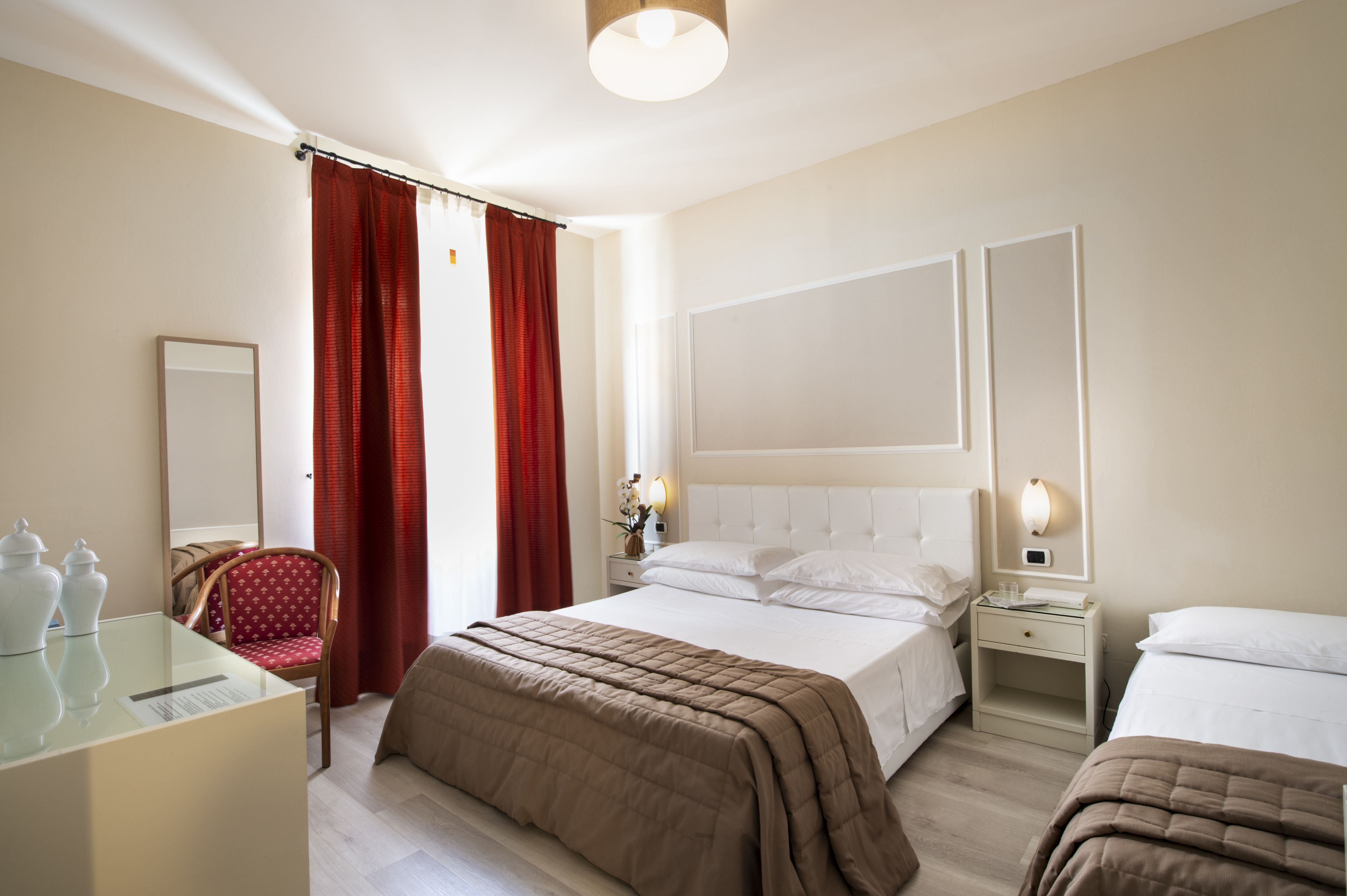 Habitación de hotel con una cama grande, una mesita de noche con lámpara, una silla y un escritorio con espejo.