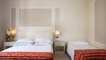 Habitación de hotel con dos camas, cada una con ropa blanca de cama y colchas estampadas en rojo. Hay mesitas de noche con lámparas y un aplique en la pared sobre las camas.