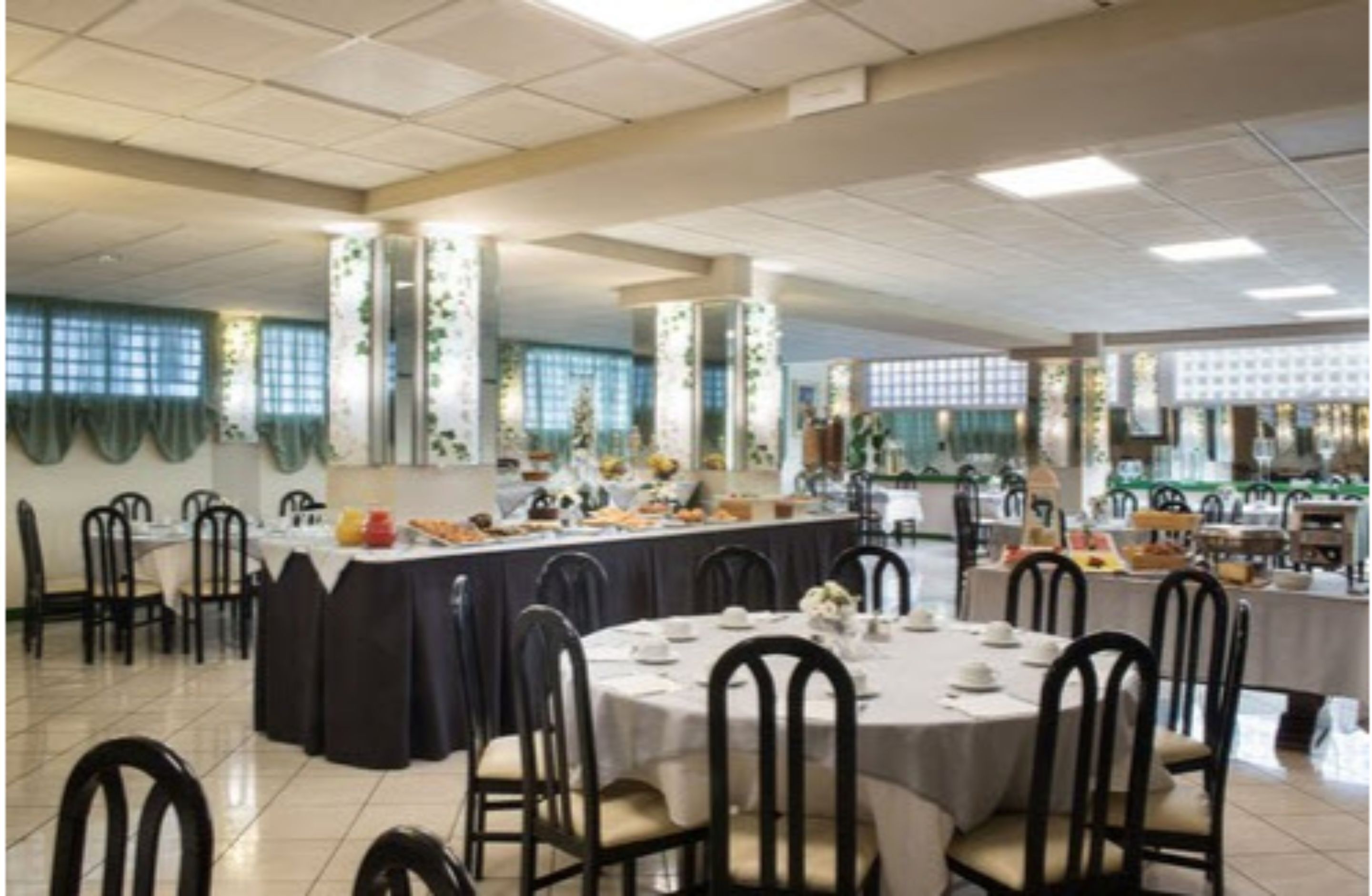 Un comedor con mesas redondas, sillas negras y un sistema de buffet.