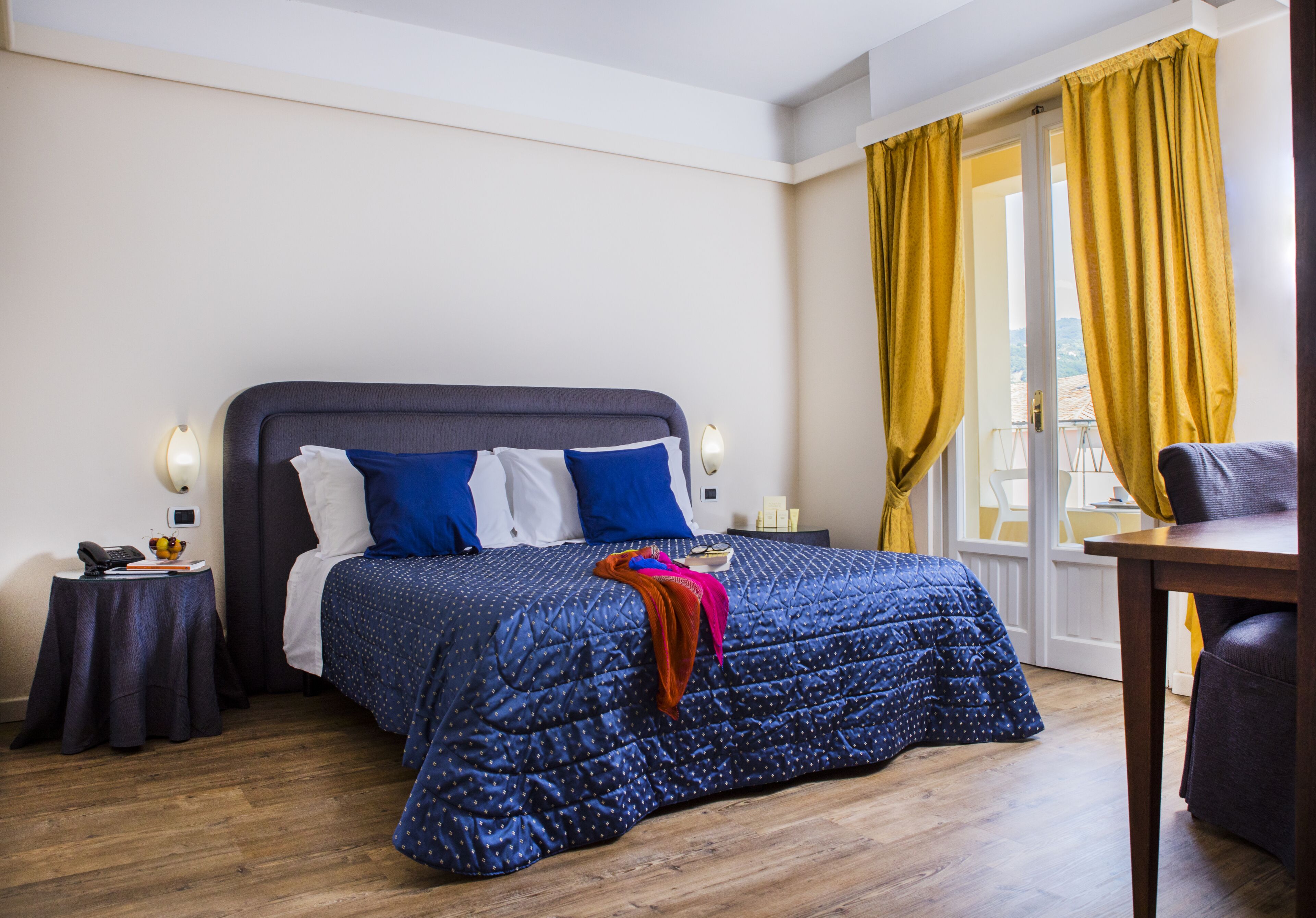 Una camera da letto con un letto grande, un comodino con una lampada, una sedia e vista all'esterno attraverso una finestra con tende gialle.
