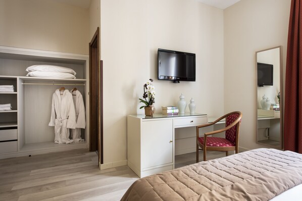 Quarto de hotel com uma cama, uma escrivaninha com cadeira, televisão, guarda-roupa e espelho.