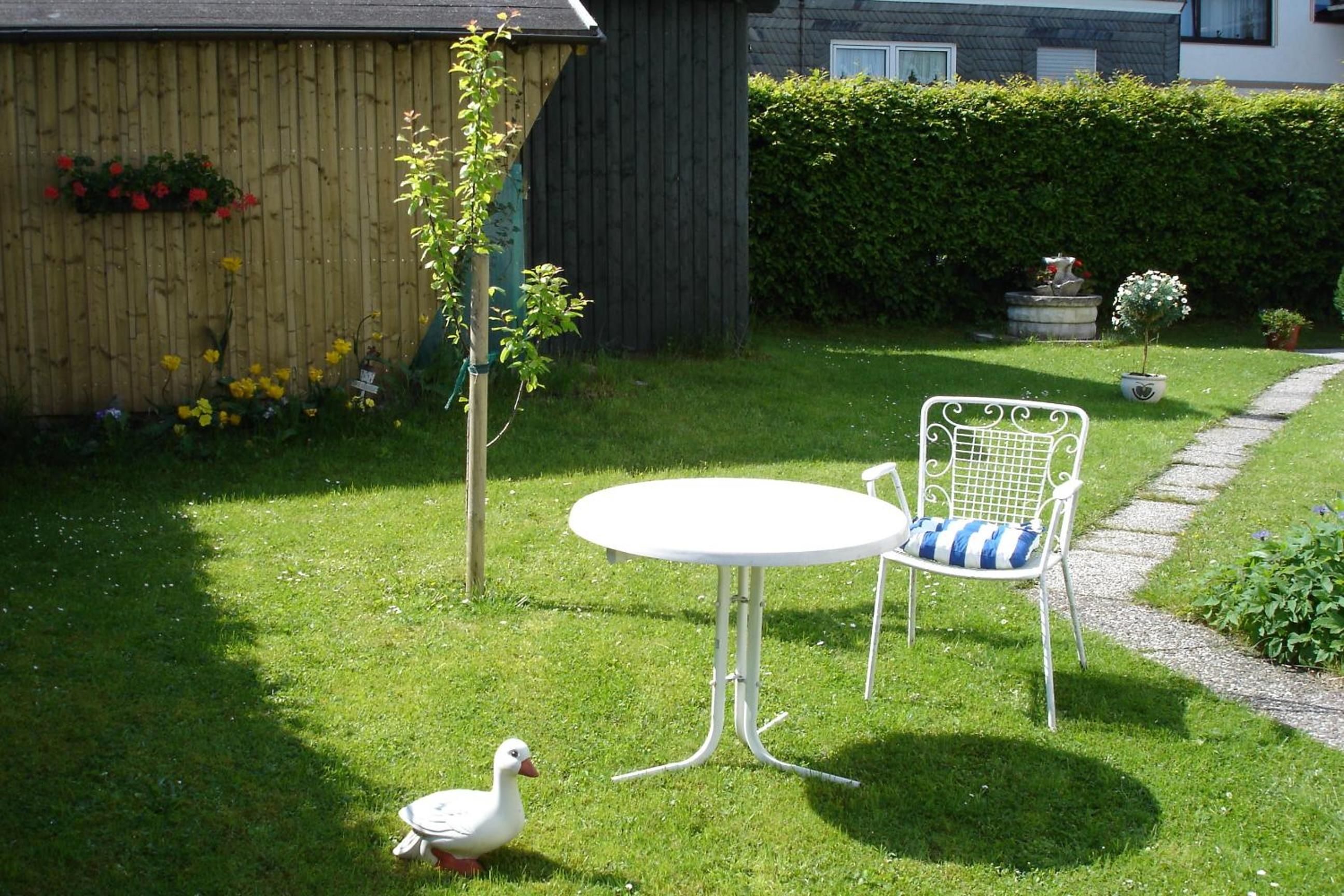 Ein Garten mit einem weißen Tisch und Stuhl, einem Holzzaun und einer Ente.