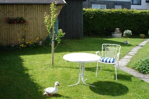 A garden with a white table and chair, a wooden fence, and a duck. - Gästehaus Tepel (Winterberg)