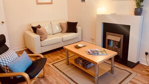 Ein Wohnzimmer mit einem weißen Sofa, einem Holztisch, einem Kamin und einer Topfpflanze.