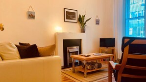 Ein Wohnzimmer mit einer Couch, einem Couchtisch, einem Kamin, einem Fernseher und einem Fenster mit Jalousien.