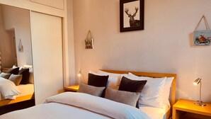 Ein ordentlich bezogenes Bett mit weißer und grauer Bettwäsche, ein Holzkopfteil und ein Nachttisch mit einer Lampe.