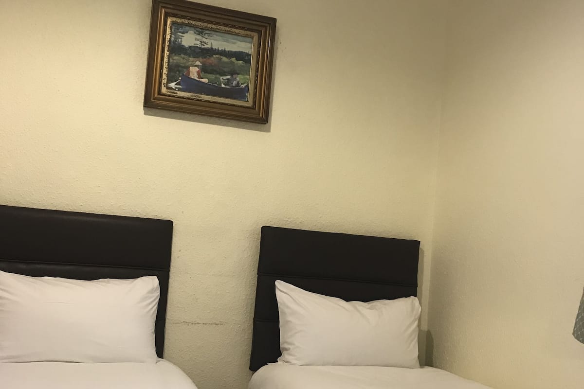 Een hotelkamer met twee bedden, elk voorzien van een wit kussen en een blauwe deken. Daarboven hangt een schilderij aan de muur.