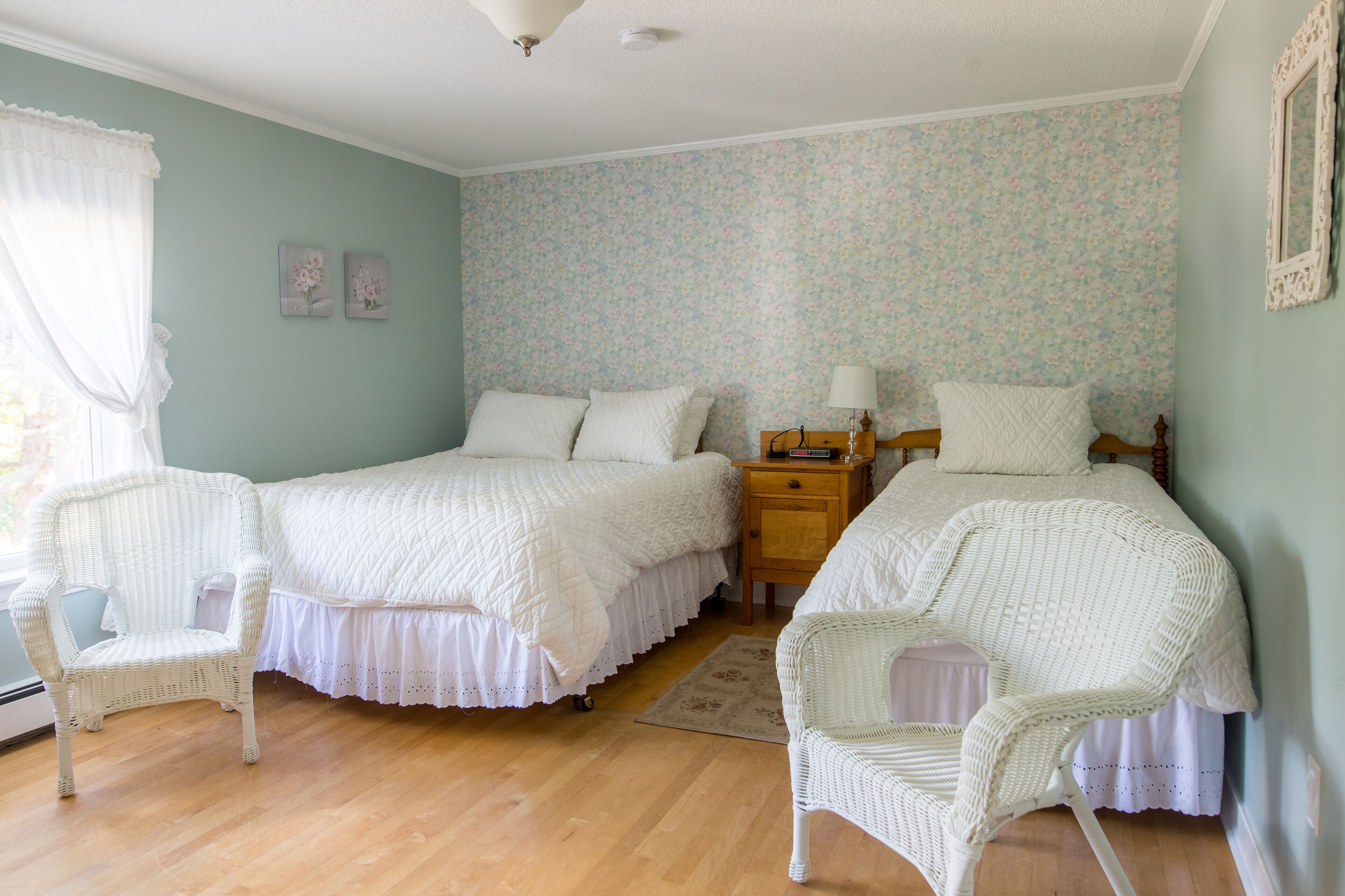A bedroom with two beds, wicker chairs, a nightstand, and floral wallpaper.
