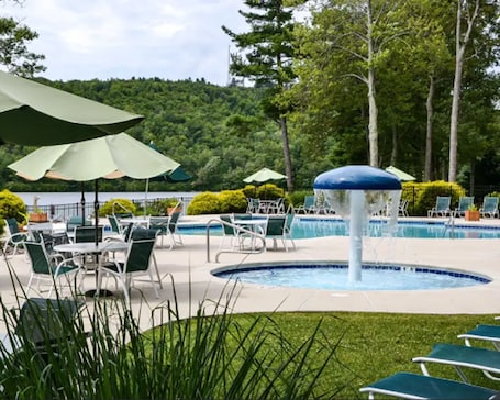 A pool area with lounge chairs and umbrellas, surrounded by greenery and trees.