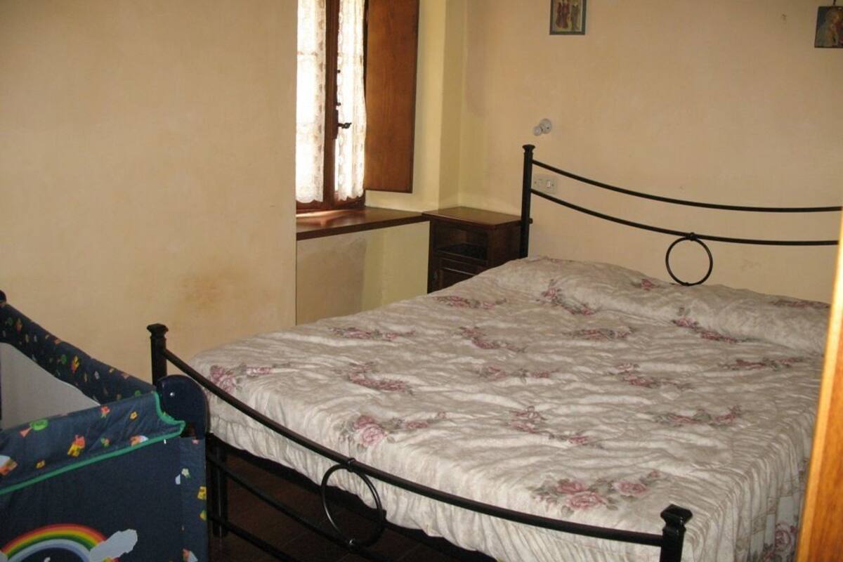 Une chambre avec un lit simple, une fenêtre avec des rideaux, une petite table de chevet et un tableau accroché au mur.