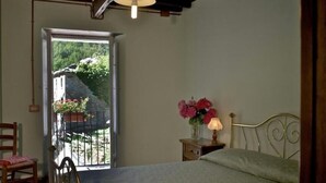 Ein Schlafzimmer mit einem Bett, einem Nachttisch mit Lampe, einem Sessel und Blick auf einen Balkon mit Pflanzen.