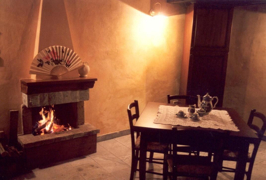 A cozy dining area with a fireplace, a table set with a teapot and cups, and a fan on the mantel.