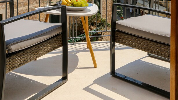 Ein Balkon mit Tisch, gedeckt mit Früchten und einem Glas Orangensaft, mit Blick auf eine historische Stadt mit Terrakotta-Dächern und einem Kirchturm.
