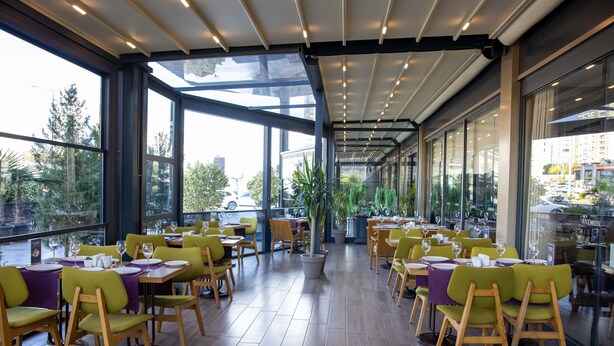 A restaurant with outdoor seating, large windows, and a view of the city. - Anemon Kent Mersin Hotel (Mersin)