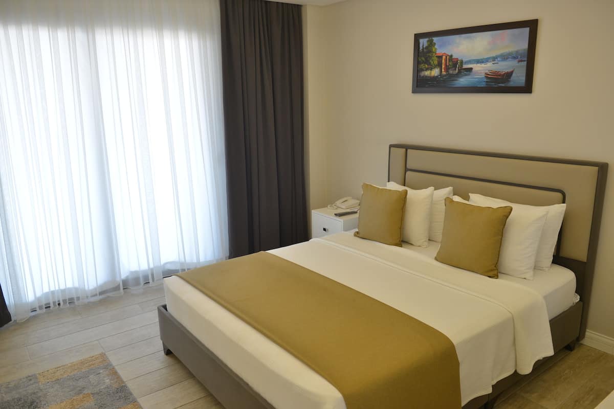 Quarto de hotel com cama, mesa de cabeceira, um quadro e janela com cortinas.