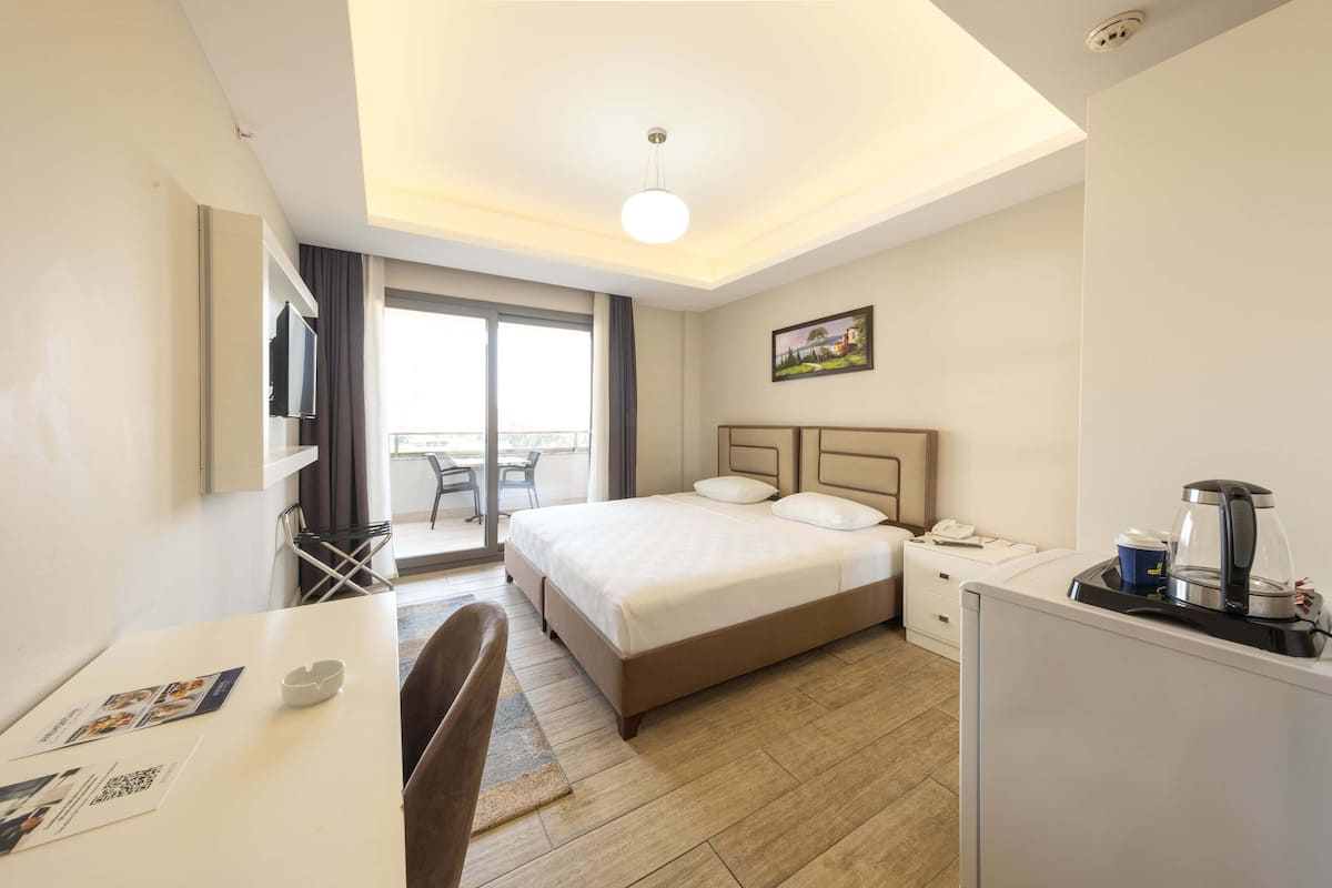 Quarto de hotel com cama, escrivaninha, cadeira, cafeteira e vista para o exterior.