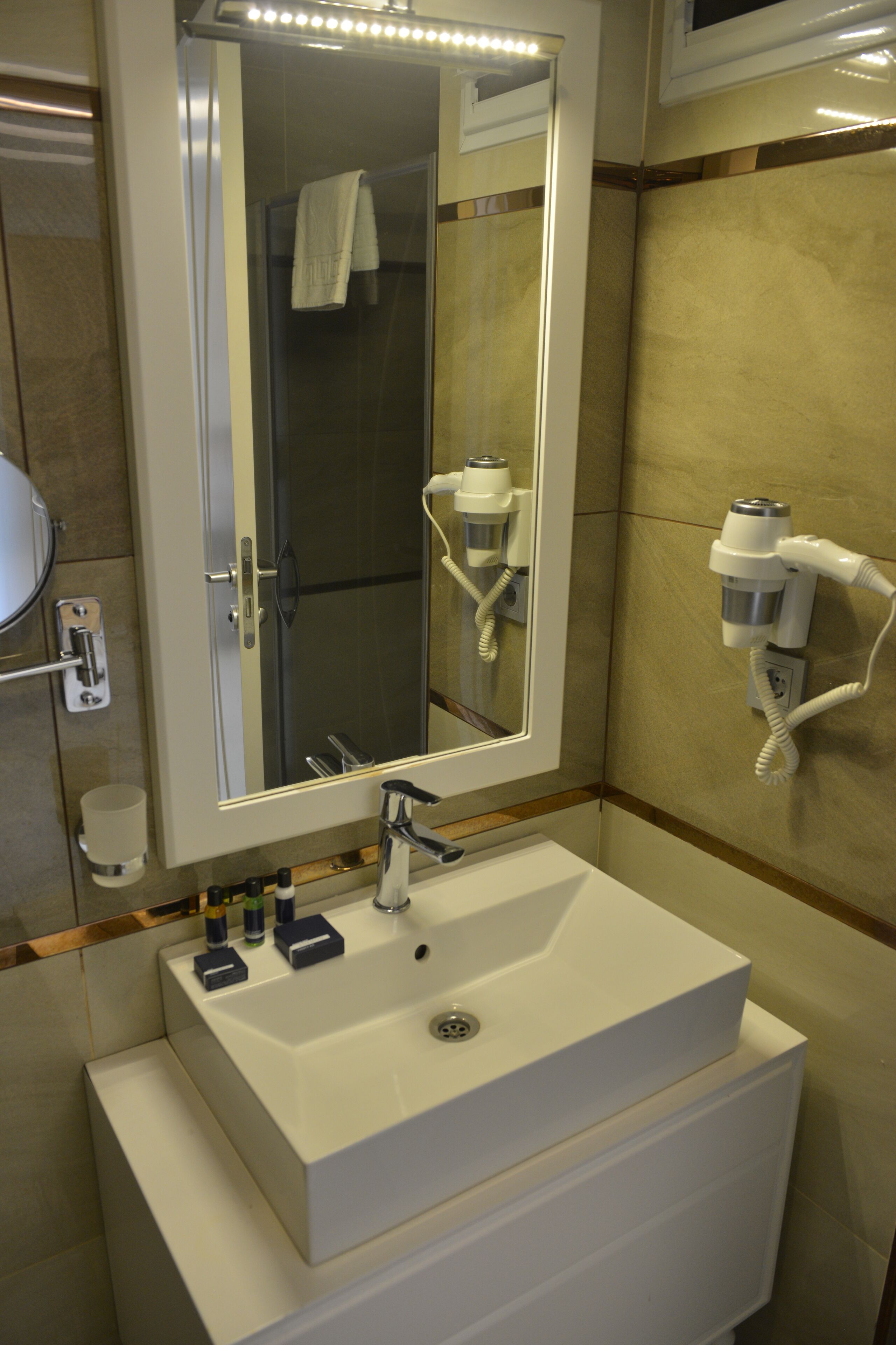 Ein Badezimmer mit einem weißen Waschbecken, einem Spiegel und einem an der Wand befestigten Fön.