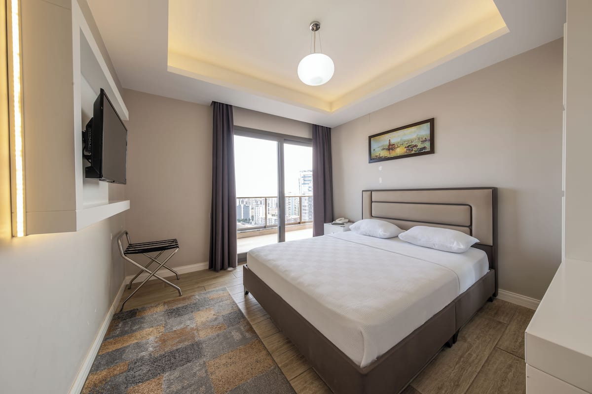 Quarto de hotel moderno com uma cama grande, televisão de tela plana na parede, vista da cidade pela janela e tapete estampado no chão.