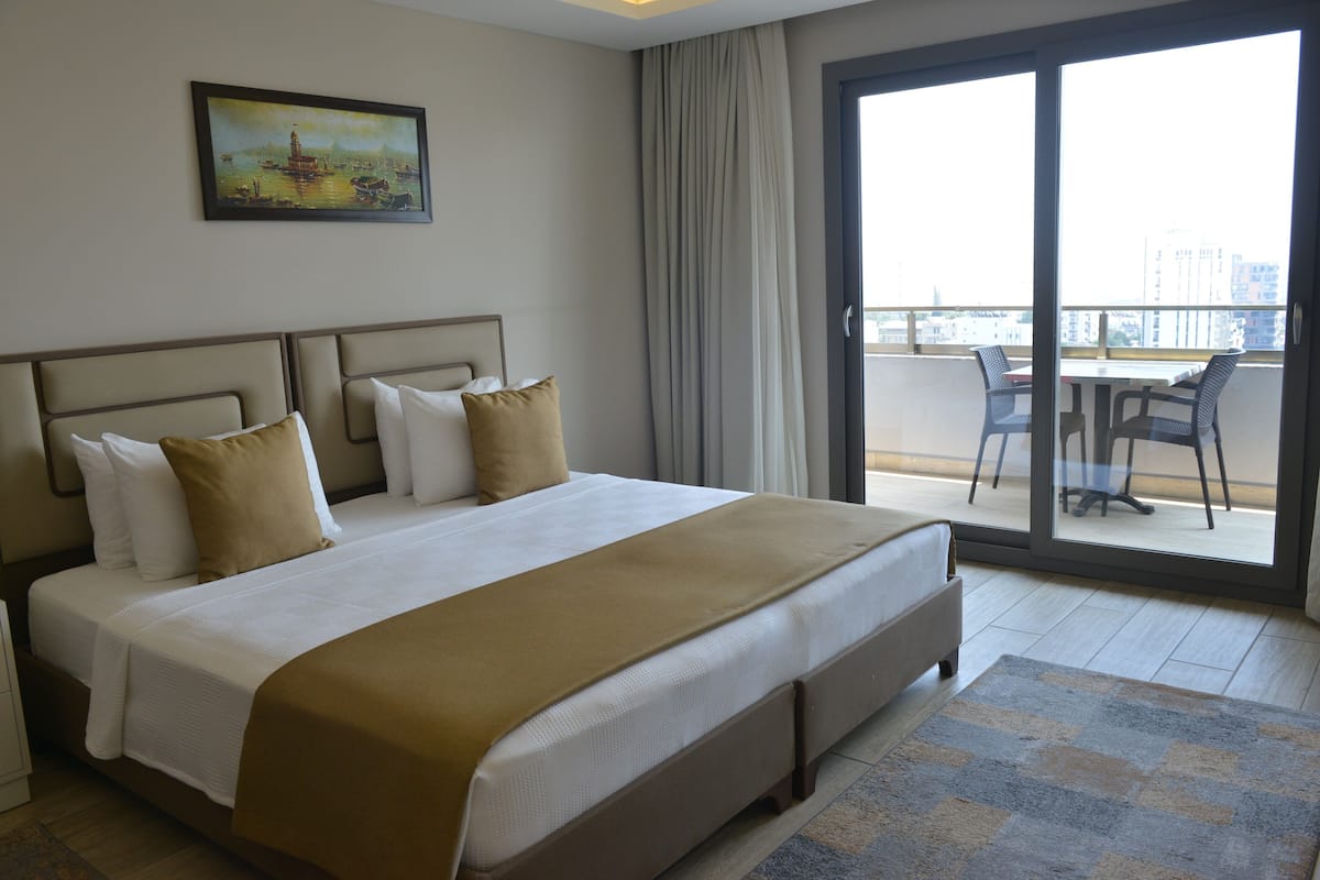 Quarto de hotel com uma cama, um quadro, uma varanda com cadeiras e vista para a cidade.