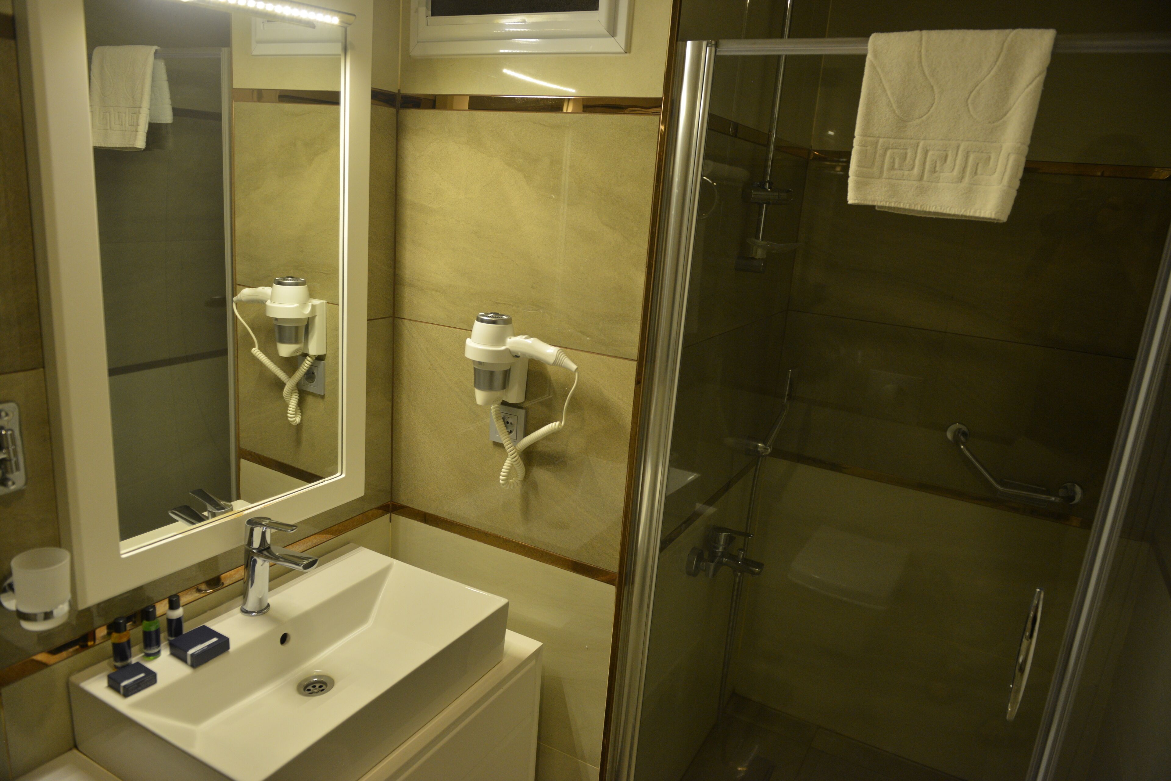 Um banheiro com pia, espelho, porta-toalhas e área de chuveiro com box de vidro.