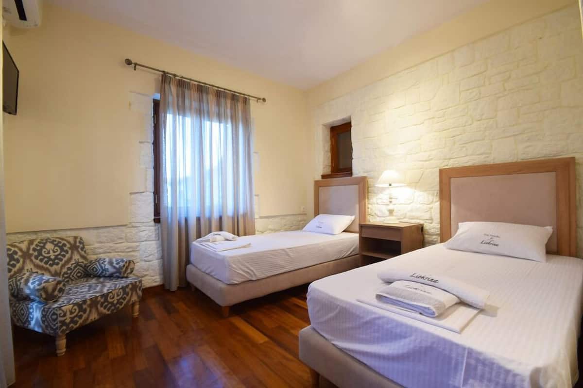 Habitación de hotel con dos camas, un sofá, una pared de piedra y una ventana con cortinas.