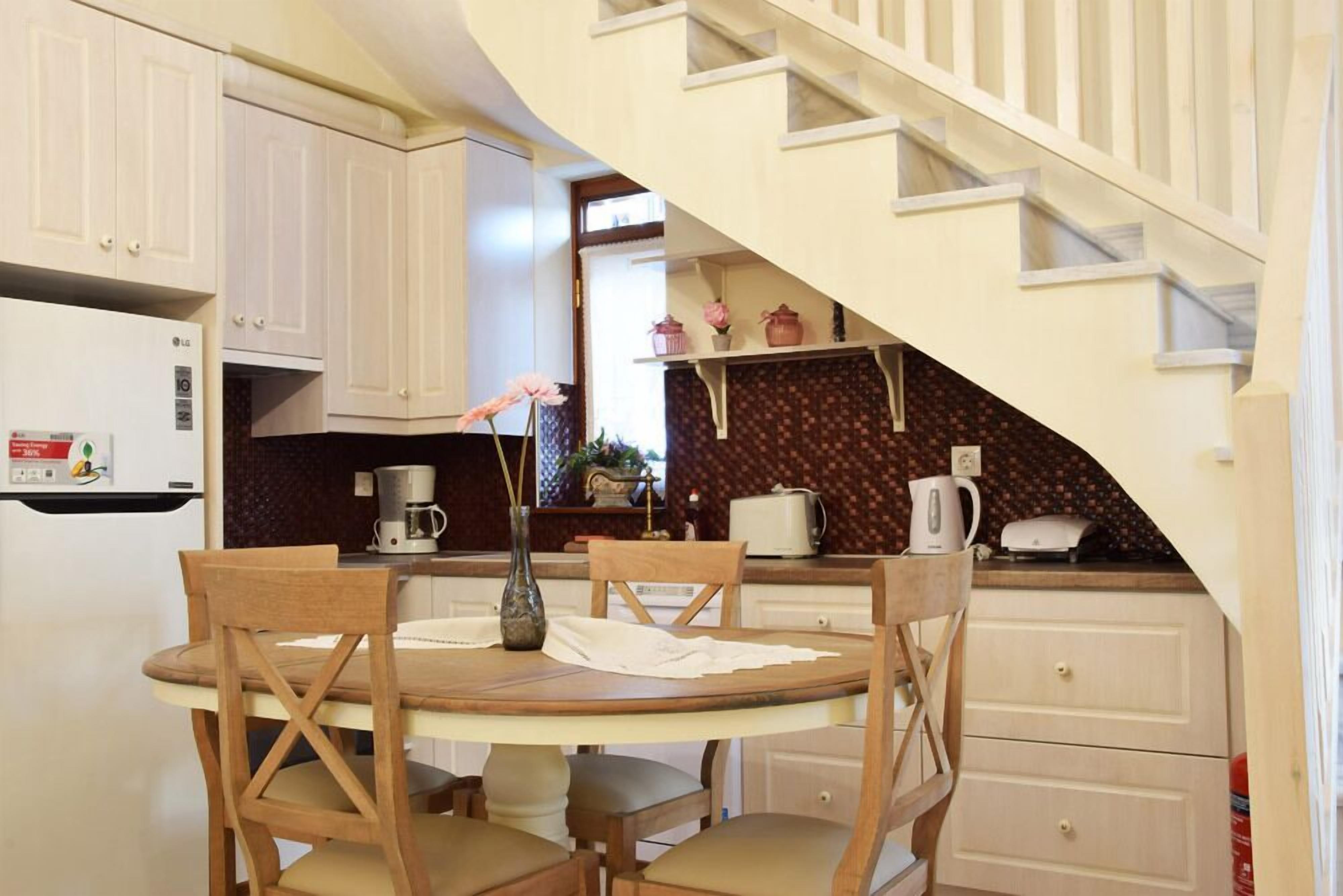 A kitchen with a dining table, chairs, a coffee maker, and a staircase.